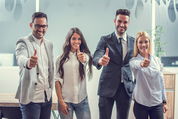 Happy business people showing thumbs up while standing in the office.