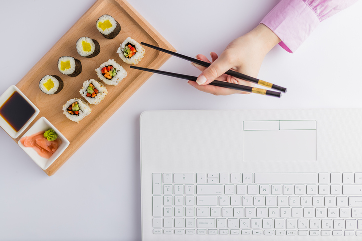 High angle view of businesswoman eating sushi next to her laptop. Take away japanese food and online order concept.