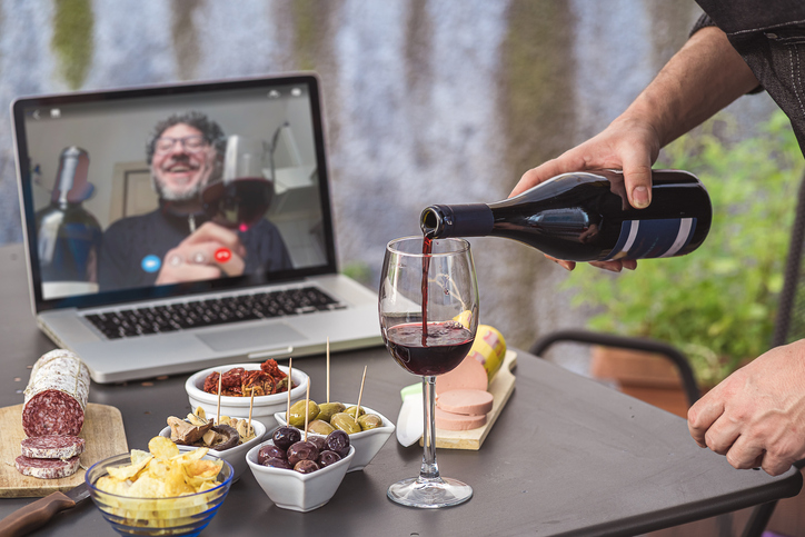 Lockdown aperitif video call party. Adult men are making a pre-meal aperitif with snacks, wine, and Italian appetizers together at home using teleconference platform apps during COVID-19 restrictions
