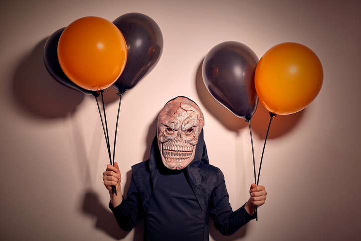 7 years old boy in halloween costume with a monster esqueleton mask holding black and orange balloons.