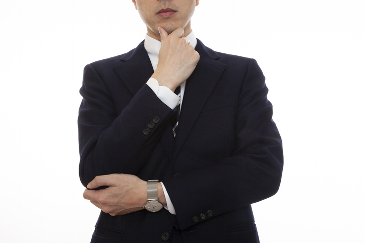 A man in a suit who makes a gesture of thinking by touching his chin with his hands, white background
