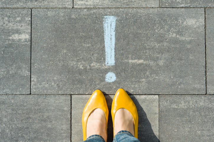 Female feet with exclamation point, symbol of attention drawn on the asphalt.