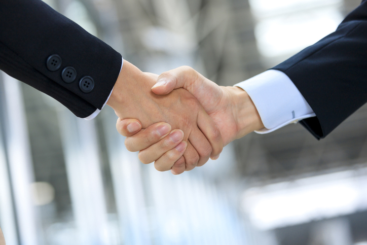 Shaking hands of businessmen and building background